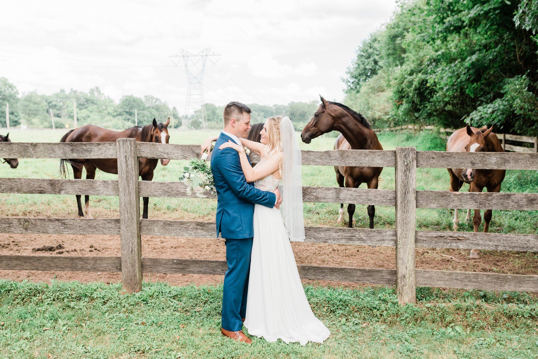 Сouple wearing a white gown and a blue suit near the horses